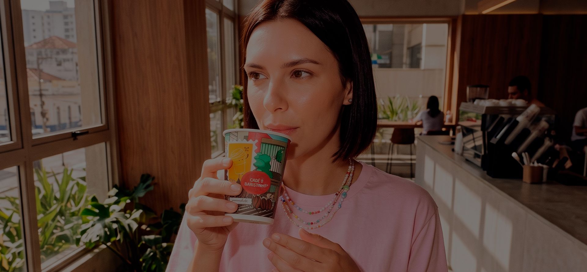 Mulher tomando café em um copo de papel personalizado numa cafeteria