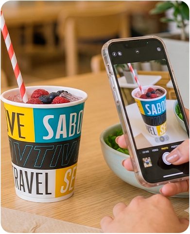 Cliente fotografando com o celular um copo personalizado sobre a mesa